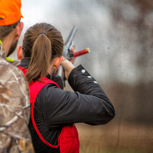 Female hunter shooting shotgun with trainer standing behind